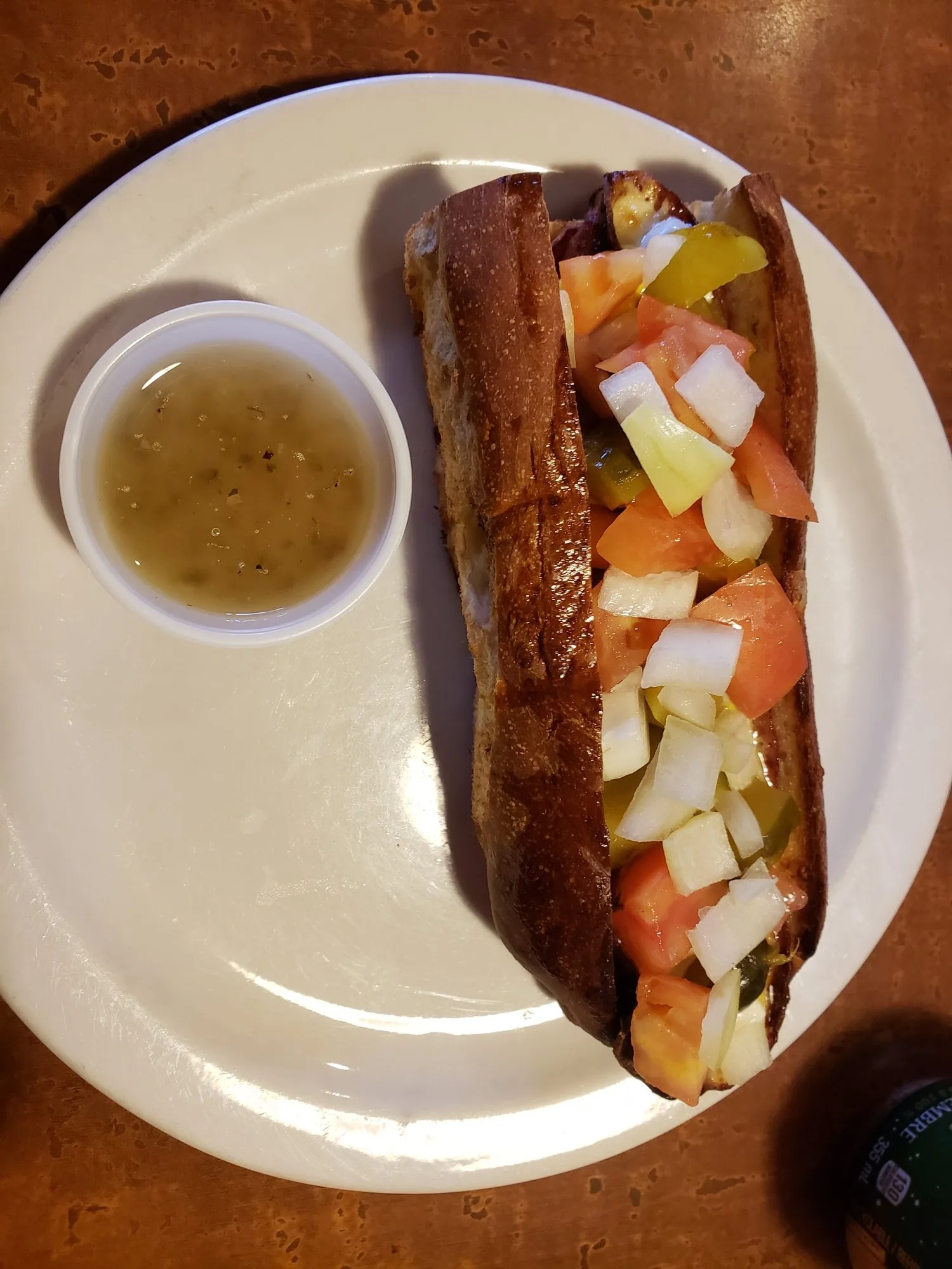 An oven-baked sub with tomato and onion and a cup of sauce on a plate