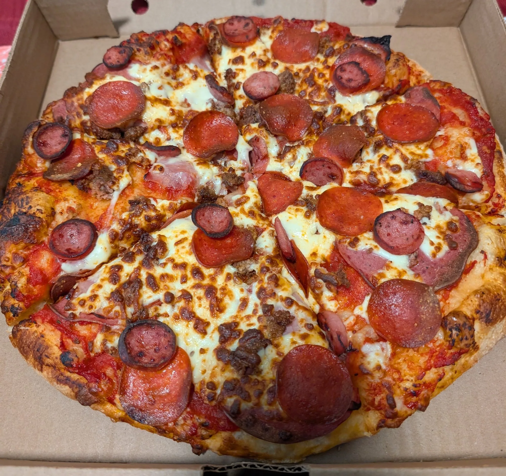 A meat pizza with pepperoni, salami and sausage in the box, seen from above