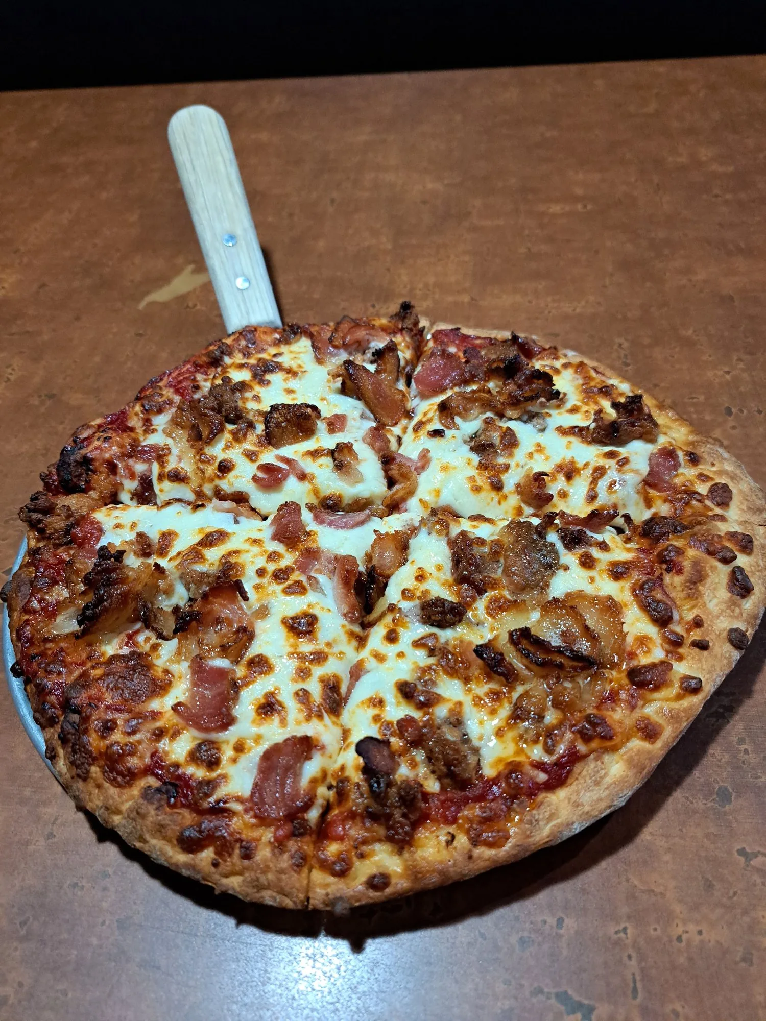 A loaded pizza on a pan with a server, served in the dining room