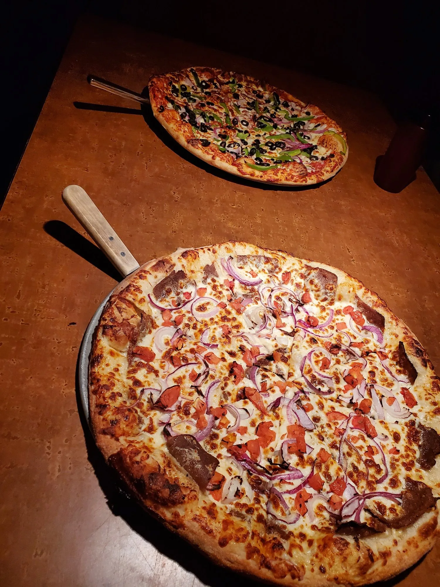 Two pizzas on metal pans on the dining room table