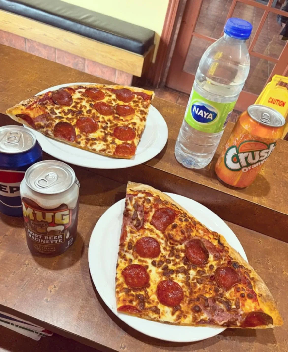 Two pepperoni slices on plates with a can of pop, a water and an orange Crush
